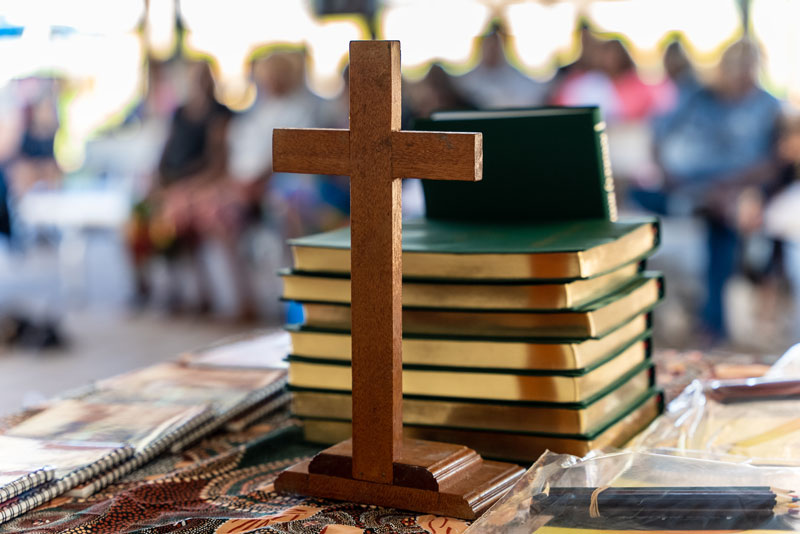 Wooden cross standing on a table in front of a stack of new Bibles